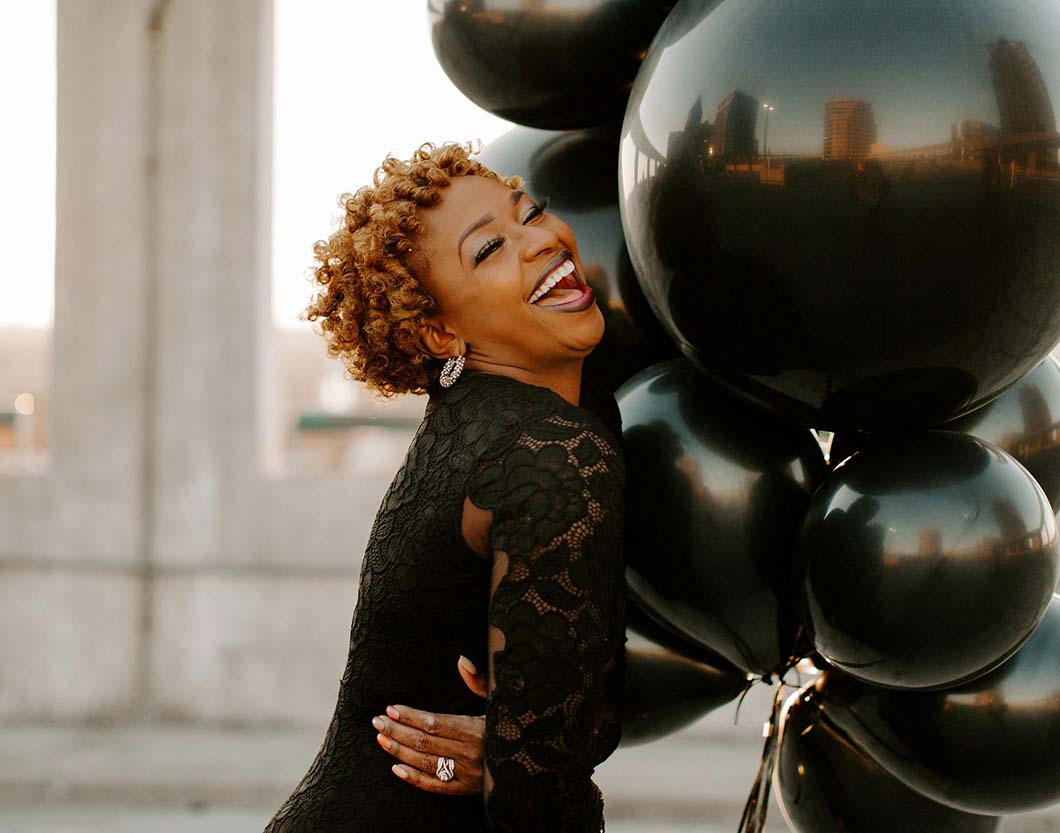 Black woman with short afro holds ballon to celebrate life despite thinning hair and perimenopause